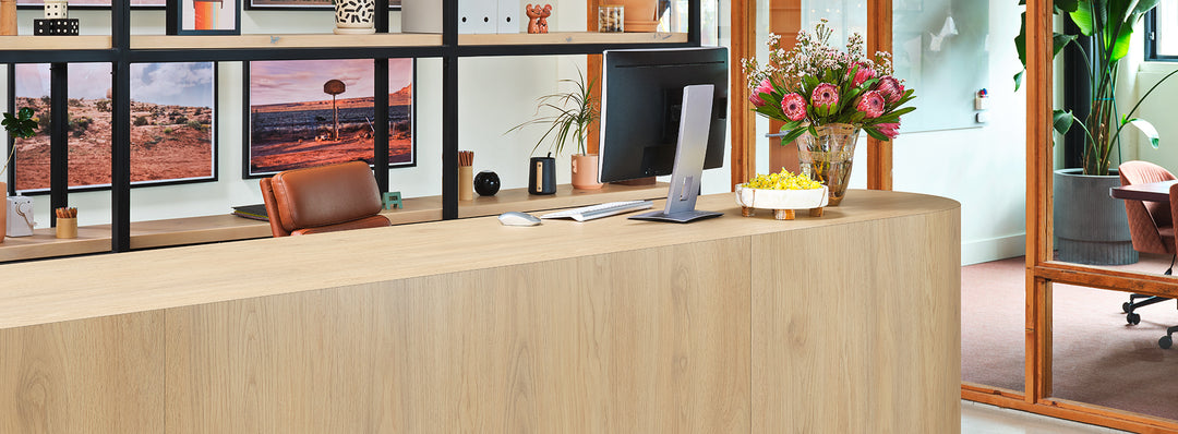 Formica Natural White Oak Wooden reception desk with computer and decor in a modern office setting